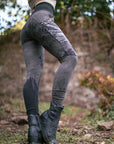 Outdoor black boots with ribbed elastic shaft, worn with a dark cap and jacket in a forest path.