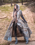 Long hooded robe in weathered grey with geometric embroidered trim and tie belt, outdoors on a path