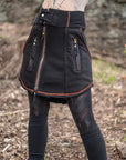 Fleece utility skirt in black with orange zipper trim and multiple front pockets, worn outdoors