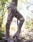 Rugged unbranded lace-up tall boots in dark brown leather, with textured sole in an outdoor woodland.