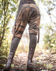 Brown lace-up knee-high leather boots with wrap straps and stitched seams outdoors in soft forest light