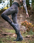 Outdoor black leather hiking boots with textured tread sole, worn in a wooded garden setting.
