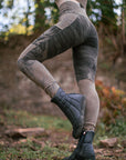 Outdoor mid-calf black rubber boots with ribbed side panels, standing in soft-focus greenery