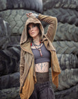 Tan zip-front hooded jacket with drawstring hem, worn outdoors against gray stone wall
