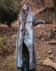 Flowing hooded cloak in slate blue with patterned hood and tie straps, shown outdoors in soft daylight